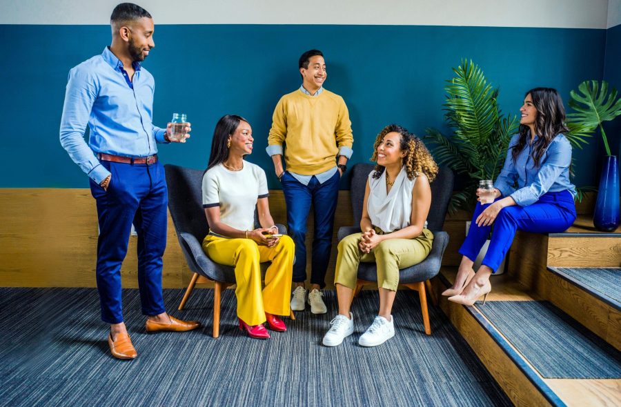 A diverse group of five professionals engaging in a casual indoor meeting, smiling and talking.